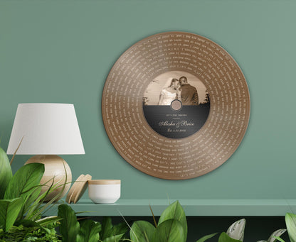 Bronze round song lyrics record on a sage green wall above a lamp and plants