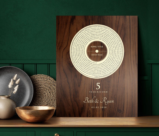 This is a photo of a 5th wedding anniversary, Our 5 Year Record wall plaque is a wood plaque - The record design pops in a natural birch tone set against a deep brown stained and polished birch - featuring song lyrics of choice in a vinyl record motif, accented with the couple's names with a heart symbol between then and the couples wedding date