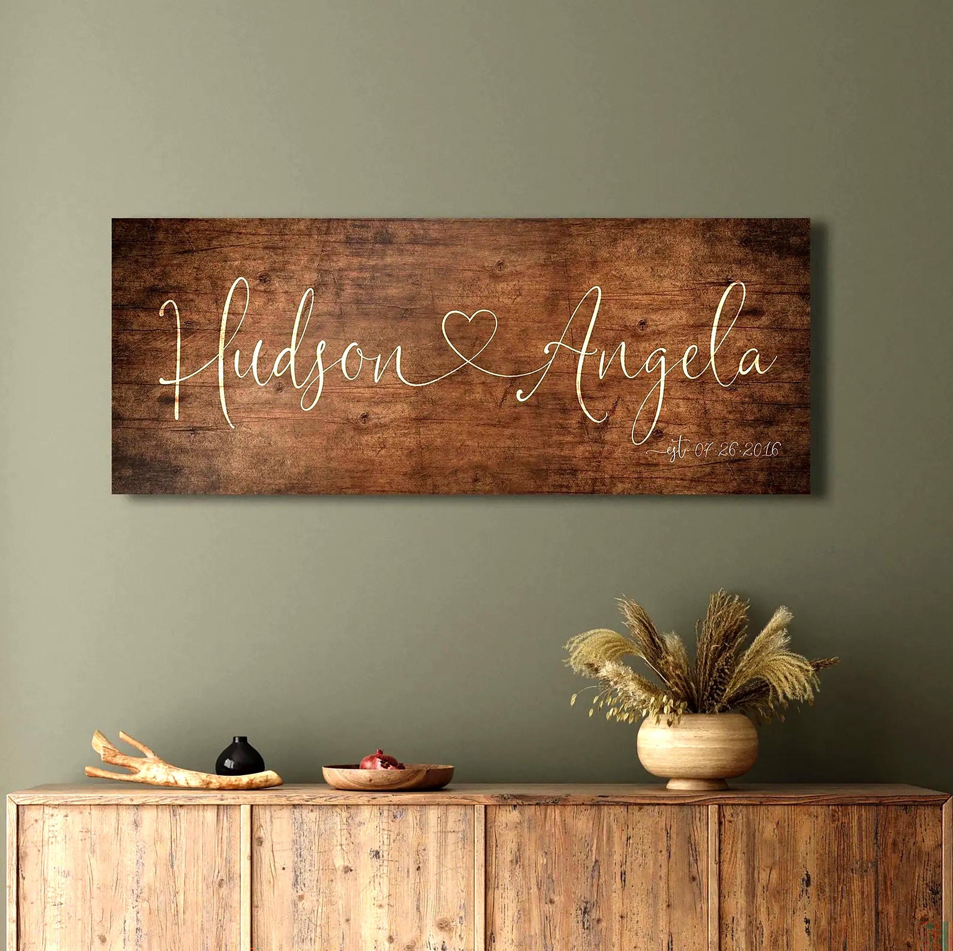 One Heart Between Us: Couples Rustic Name Sign
A rustic wood sign featuring the names of a couple in whimsical calligraphy, connected by a single heart, hangs above a sideboard in a distressed aged birch finish. 
Courtesy of Honeycomb Proverbs