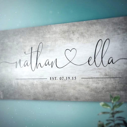 A closeup shot of tarnished name sign on tin for couples. Also features an established date beneath the names. The names are Nathan and Ella and are in a lower-case calligraphy, connected by a whimsical heart.  Photo courtesy of Honeycomb Proverbs