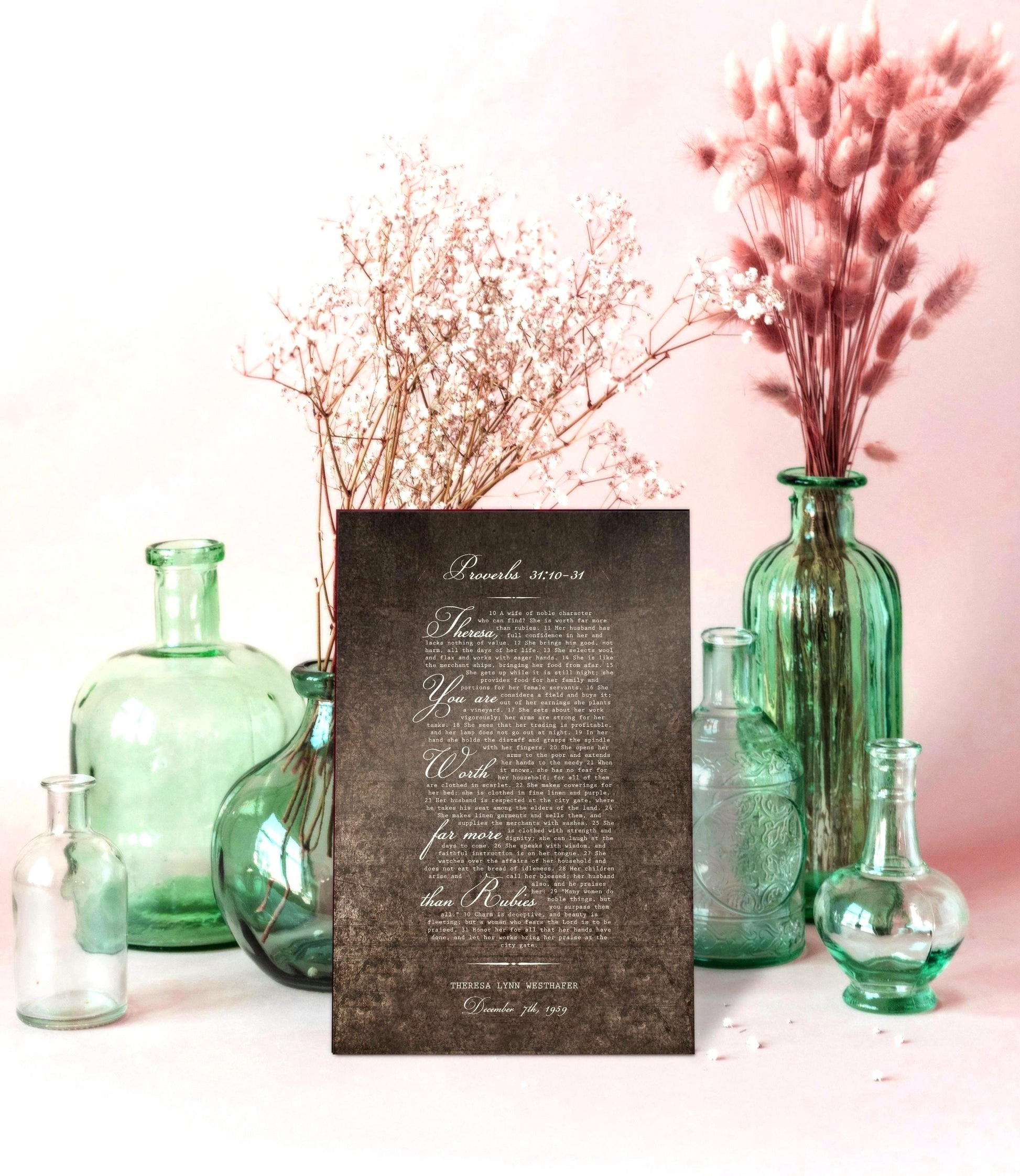 A burnished metal sign with a white inscription of a Bible verse from Proverbs 31:10-31. The text reads "Lora, you are worth far more than rubies." The date "December 25th, 2019" is printed at the bottom.