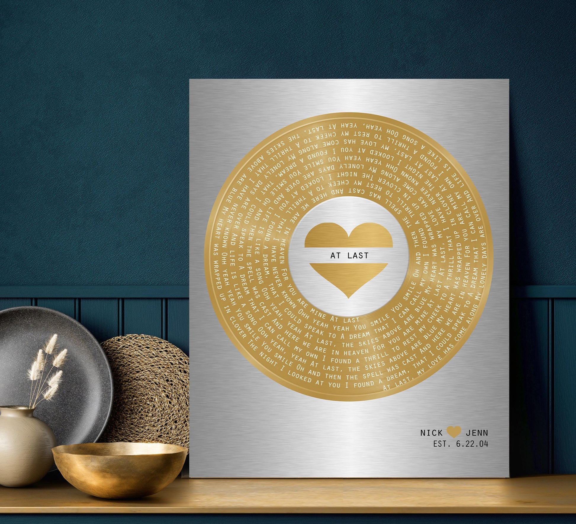 Minimalist and modern brass and tin song plaque for couples is pictured and features the song lyrics of choice with a heart inscribed motif in its center.
On the bottom right corner of the plaque sits the names of a bride and groom and their union date, making this their 21st wedding anniversary. Perfect for a brass themed gift.

Metal plaque photo courtesy of Honeycomb Proverbs