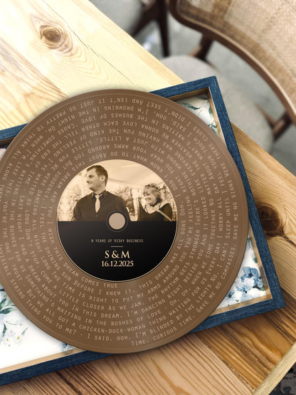 Bronze round song lyrics record with couple photo and names, shown on a wooden table