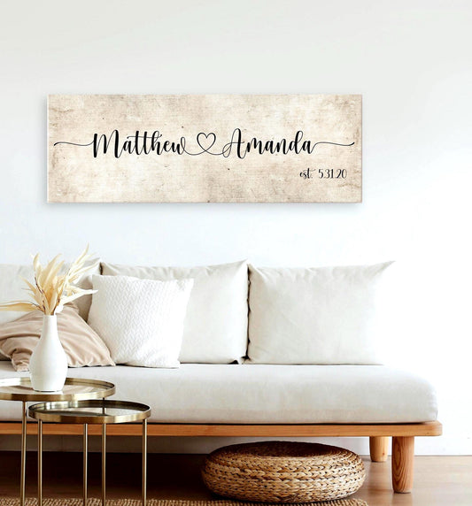 rustic cotton canvas name sign, with 2 first names connected by a heart in a whimsical and playful typeface. A personalized name sign on vintage cotton hangs on wall above bench in entry of home.