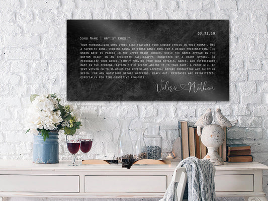 distressed, iron metal song, lyrics, sign with song lyrics, formatted in a paragraph in an orator style type face. First dance lyrics are used in the song name, and the performing artist is featured on the upper left corner and the date of their first dance is on the upper right. On the bottom, right their names are connected by a heart in a whimsical calligraphy type face. All of the inscription and lettering is done in silver and on a distressed black metal background.