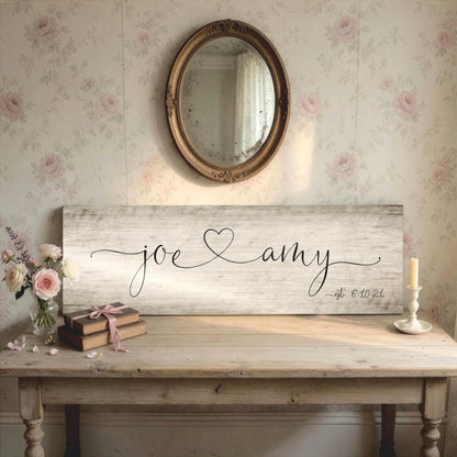 Rustic chic personalized sign on wood features the names Joe and Amy in a whimsical calligraphy with a heart connecting the names. The established date is inscribed on the bottom corner, indicating their wedding date.