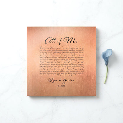 Copper song plaque with All of Me lyrics, couple's names and union date on marble beside a blue lily, 7th anniversary