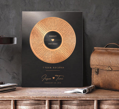 Distressed copper song record art with lyrics and a heart joining names, on a tabletop by a leather bag, 7th anniversary