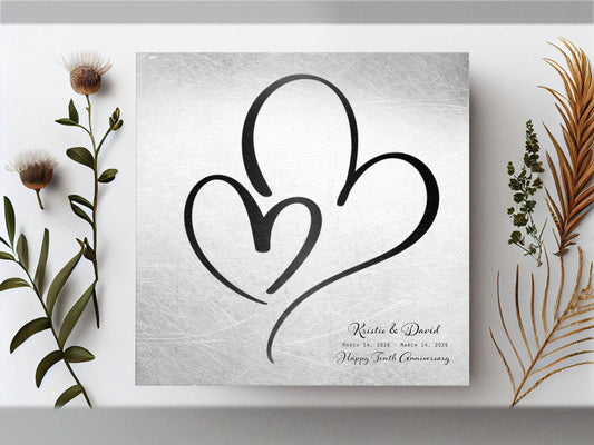 Couples Tin Hearts Distressed Anniversary wall plaque features an elegant black-toned larger heart enveloping a delicate smaller black-toned heart. Plaque includes personalization of first names, and a Happy Tenth Anniversary Wish on the bottom right. Wedding date to Anniversary date is highlighted beneath the couples names.