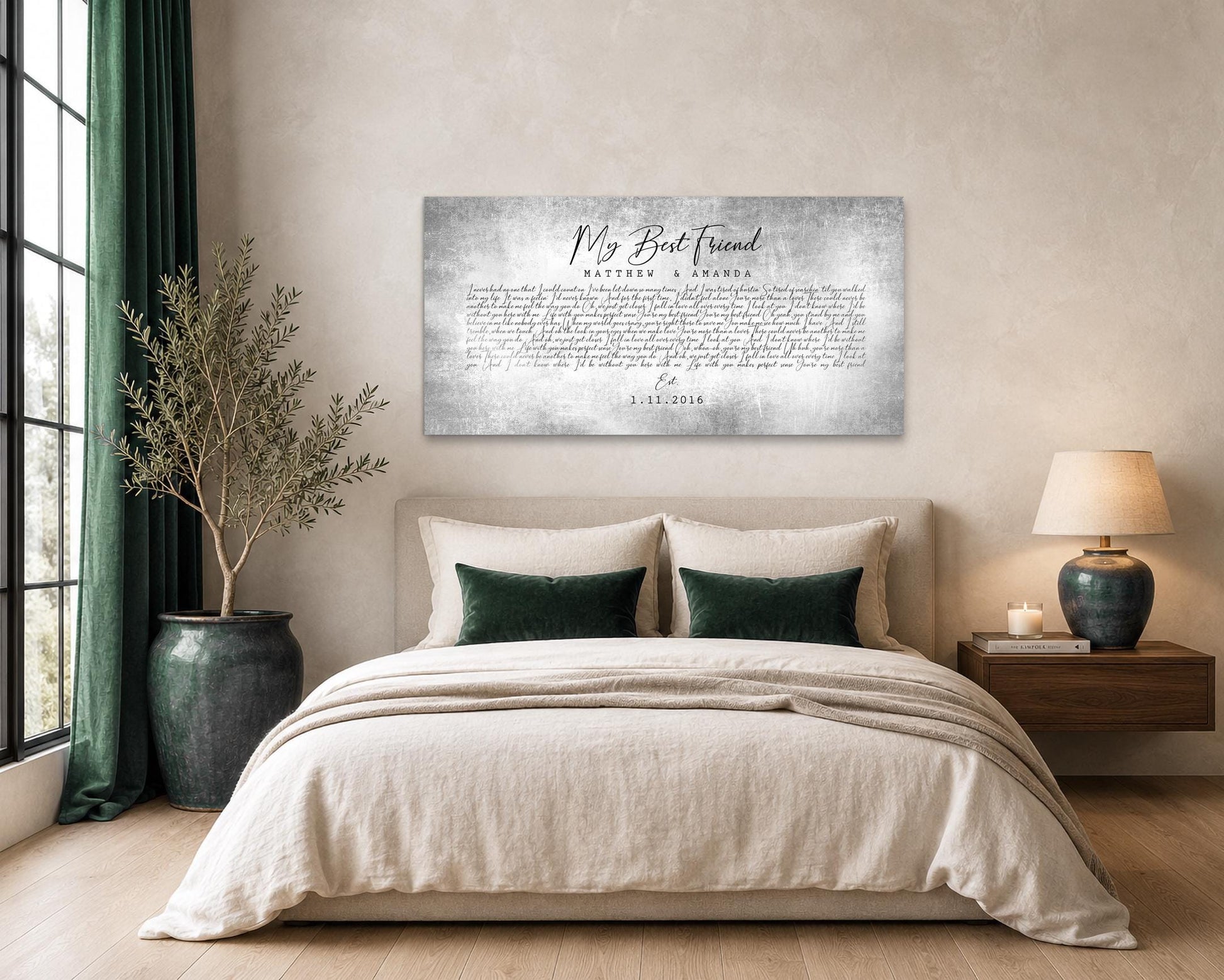 A tin and aluminum metal wall hanging is inscribed with custom song lyrics, a couple's names and an established date of the couple and is tarnished and aged looking. Art hangs above the headboard of a queensized bed in a modern sophisticated setting.