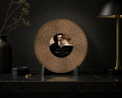 Bronze round song lyrics record with couple photo, displayed on a dark wall beside a brass lamp