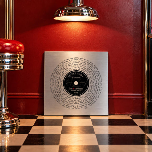 Rockabilly retro themed custom vinyl record song art on metal leans against a red wall, set on a checkerboard black and white floor.
